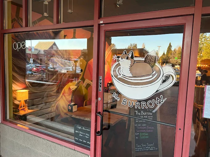 Glass door of a cafe named 'The Burrow' with a fox illustration on the window.